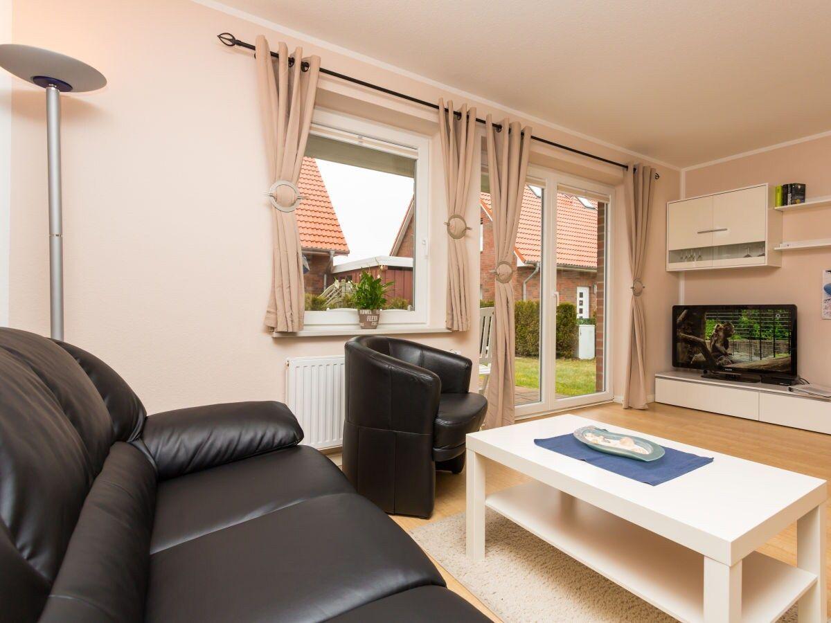 Wohnzimmer mit Sofa, Sessel, Couchtisch und TV. Durchgang zur Terrasse mit Blick auf Garten.