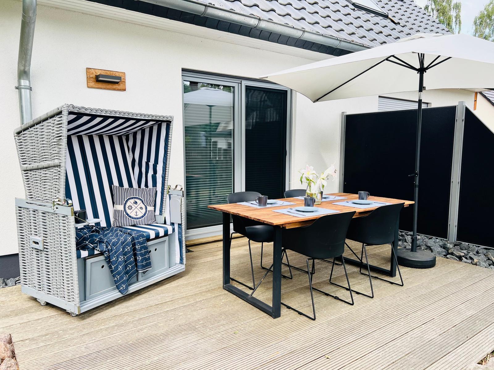 Terrasse mit Strandkorb, Tisch und Stühlen unter Sonnenschutz.