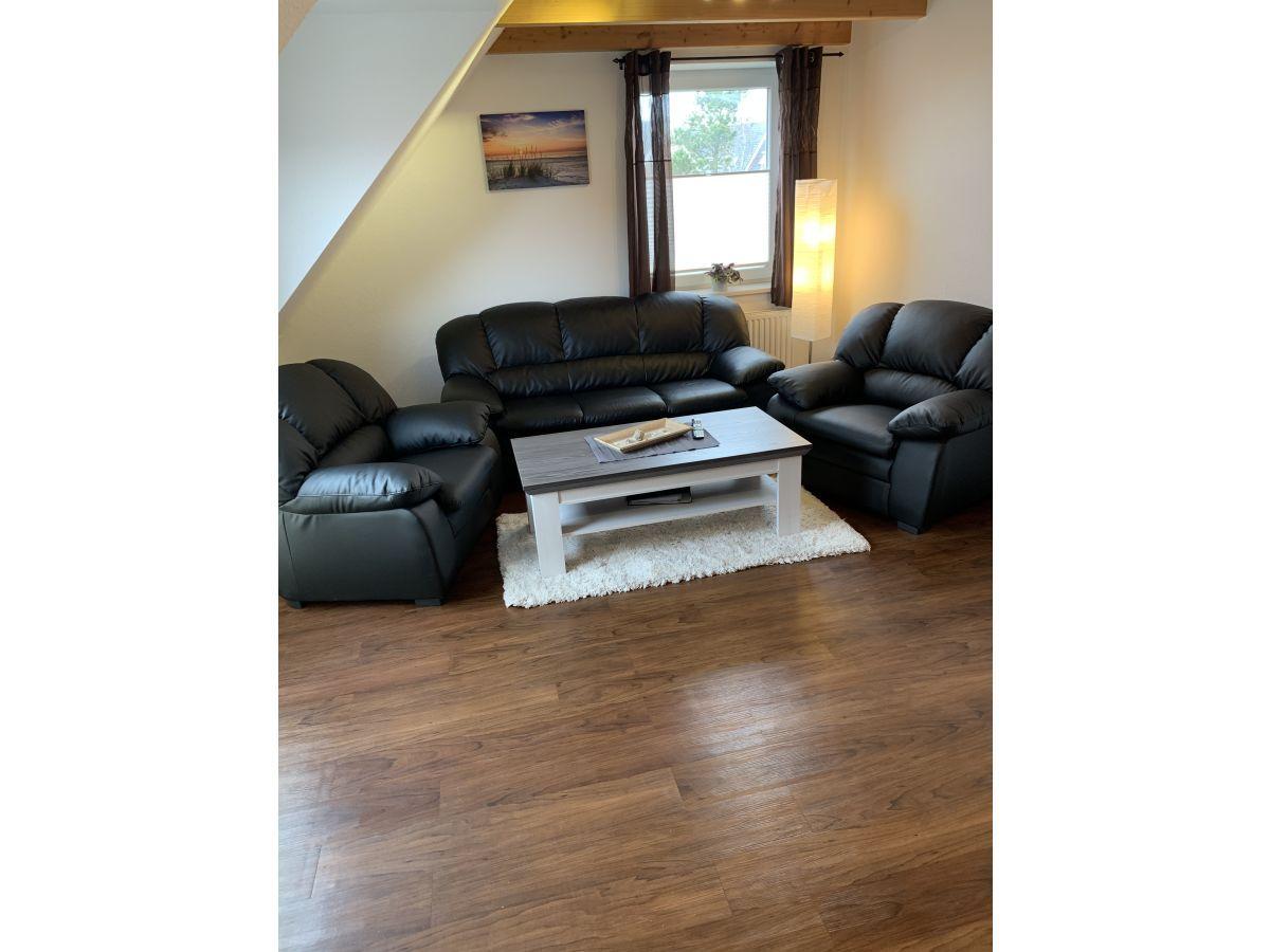 Wohnzimmer mit drei schwarzen Ledersitzen, weißem Couchtisch und Holzboden.