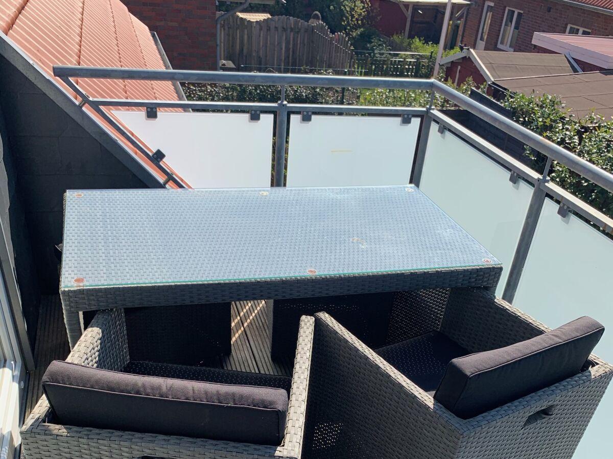 Terrasse mit Tisch und Stühlen, Glasgeländer und Blick auf Nachbarhäuser.