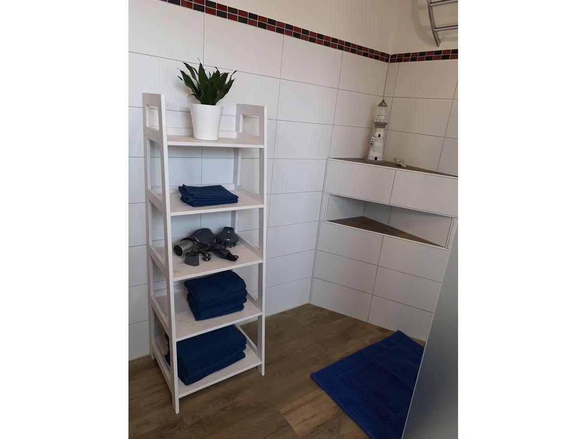 Badezimmer mit weißen Wänden, blauen Handtüchern und Pflanze auf Regal.