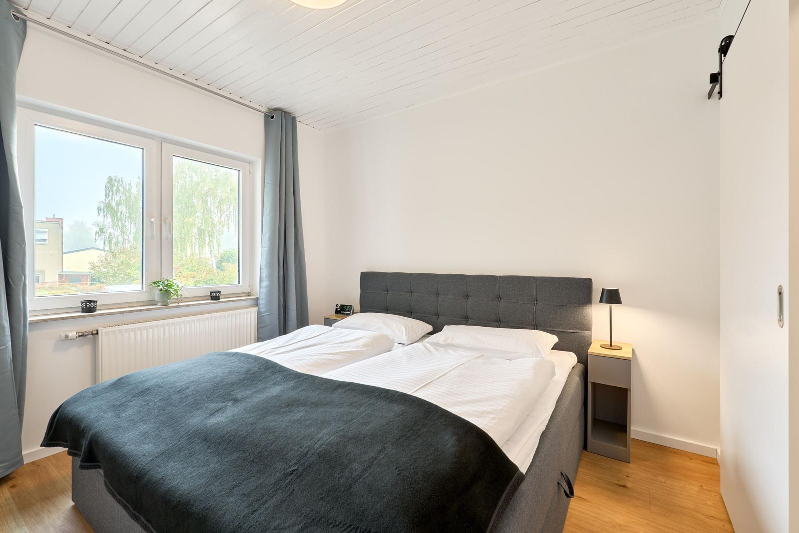 Schlafzimmer mit Doppelbett, Fenster und Nachttisch.
