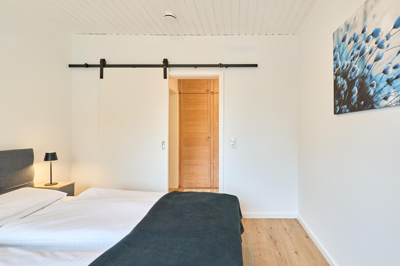 Schlafzimmer mit Bett, Schiebetür und Wandbild