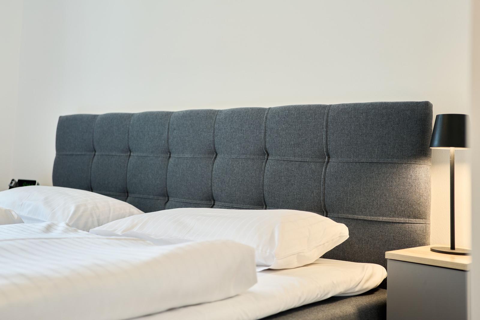 Doppelbett mit grauem Kopfteil und weißen Kissen