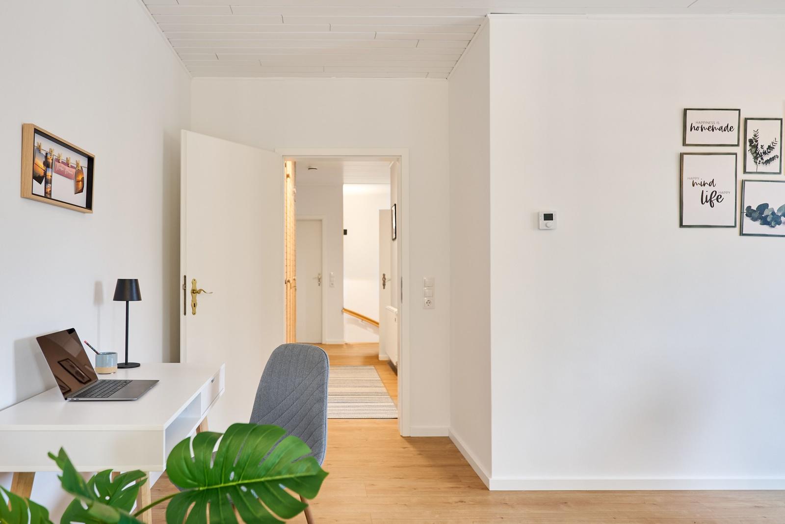 Helle Wohnung mit Arbeitsplatz, Pflanze und Bildern an der Wand.