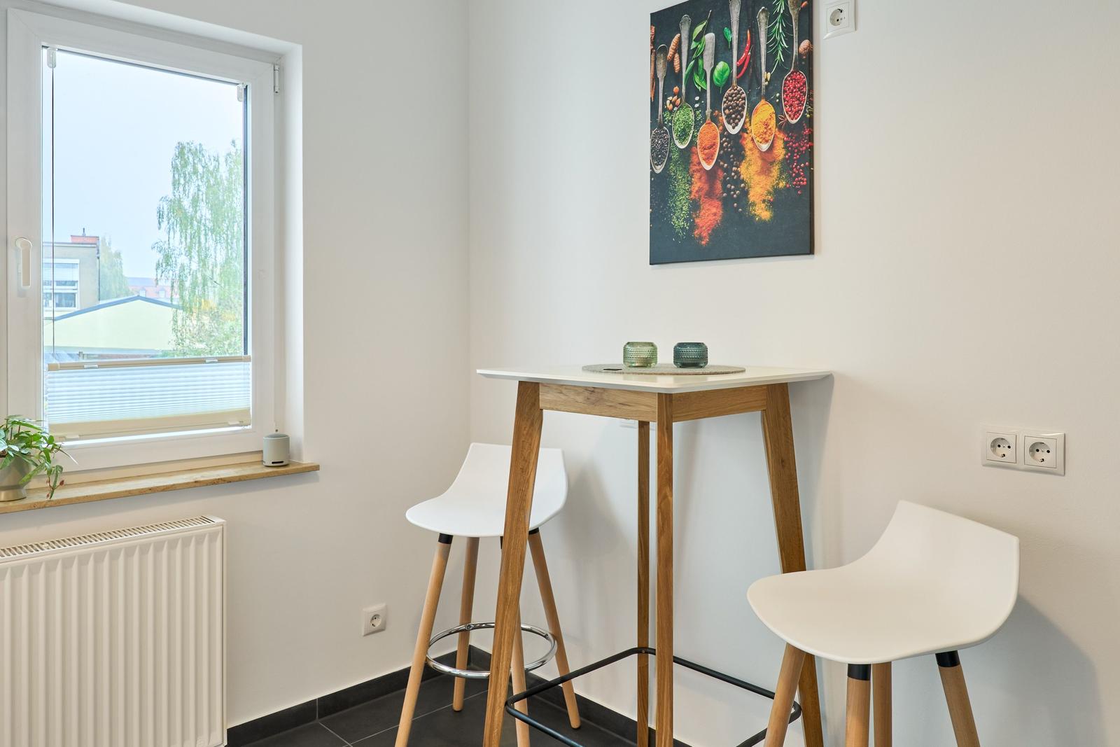 Hochwertiger Esstisch mit zwei Stühlen neben Fenster. Wandbild mit Gewürzen.