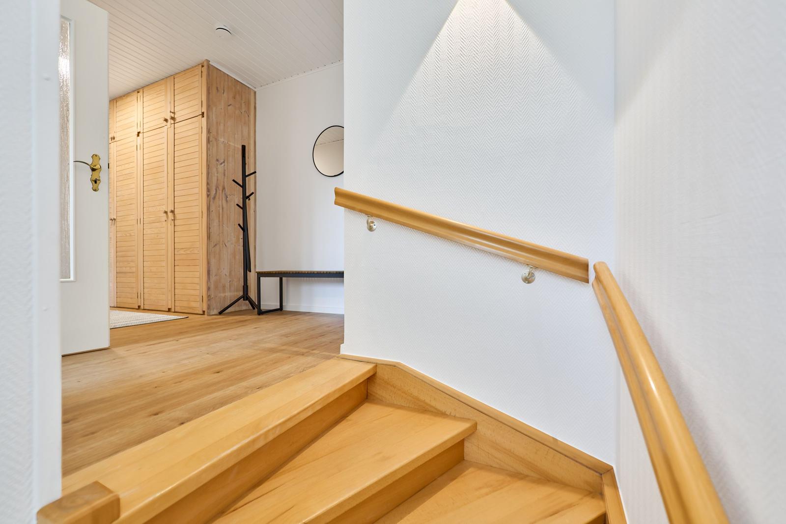 Holzgetäfelte Treppe mit Handlauf führt in ein Zimmer mit Holzschrank und Kleiderständer.