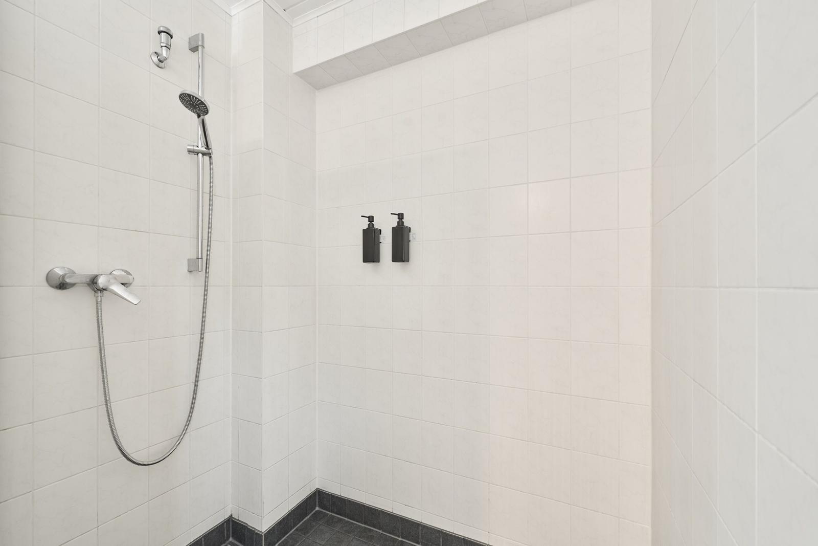 Dusche mit Duschbrause, Wandhalter und zwei schwarzen Flaschen.