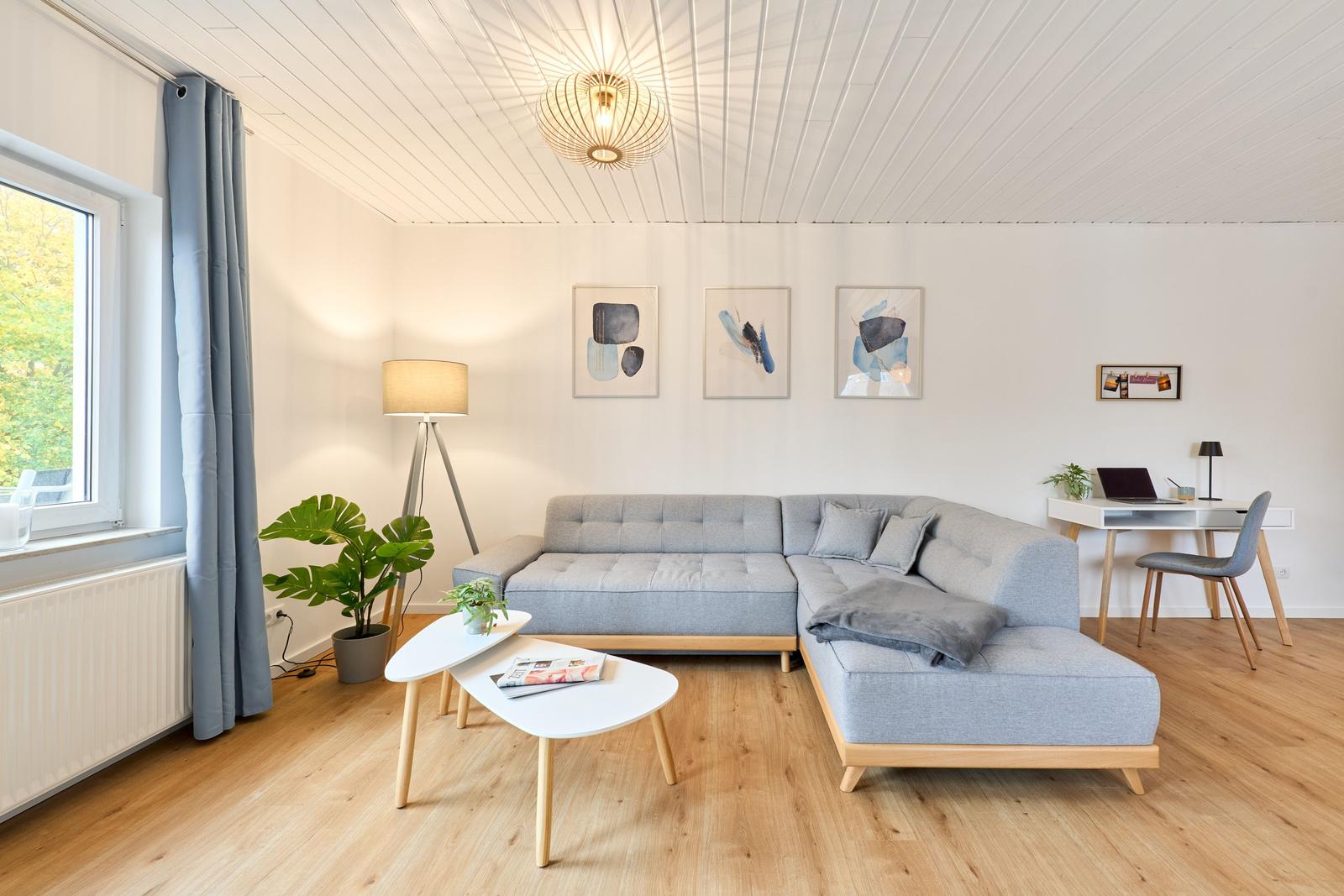 Wohnzimmer mit grauem Sofa, Holzboden und Fenster mit Blick auf Grün.