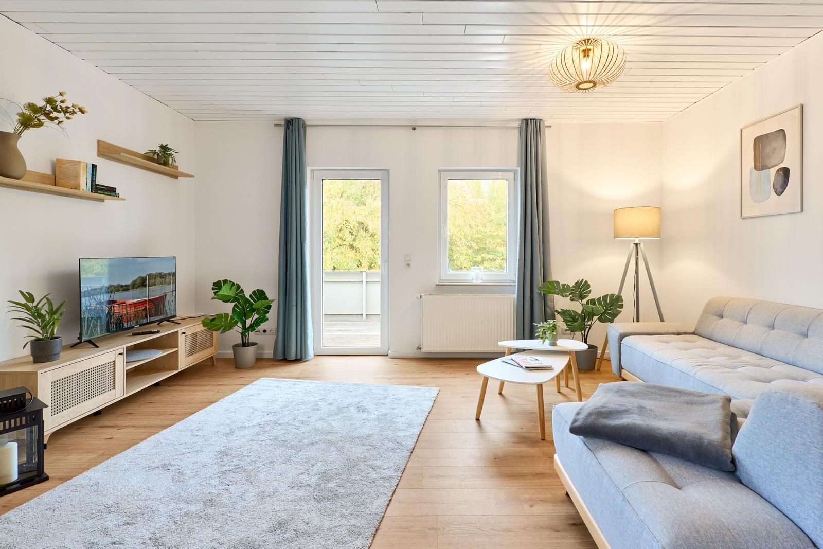 Wohnzimmer mit Sofa, Fernseher und Fenster zur Terrasse.