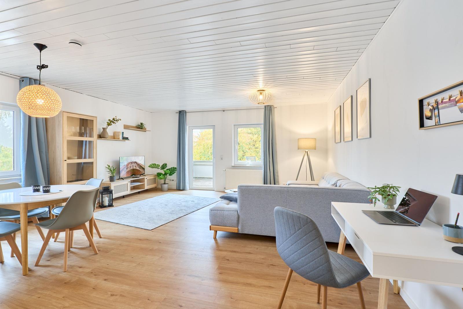 Wohnzimmer mit Essbereich, Sofa, Schreibtisch und Balkonzugang.