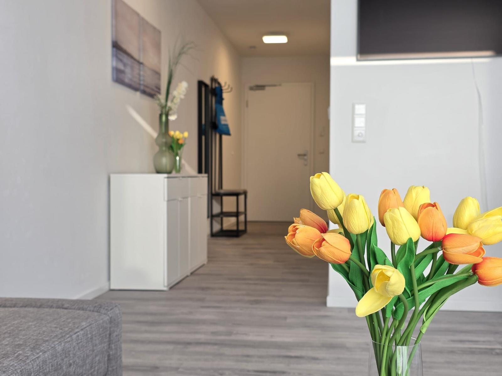 Vorraum mit Blumen und moderner Einrichtung. Hintergrund zeigt Flur und Tür.