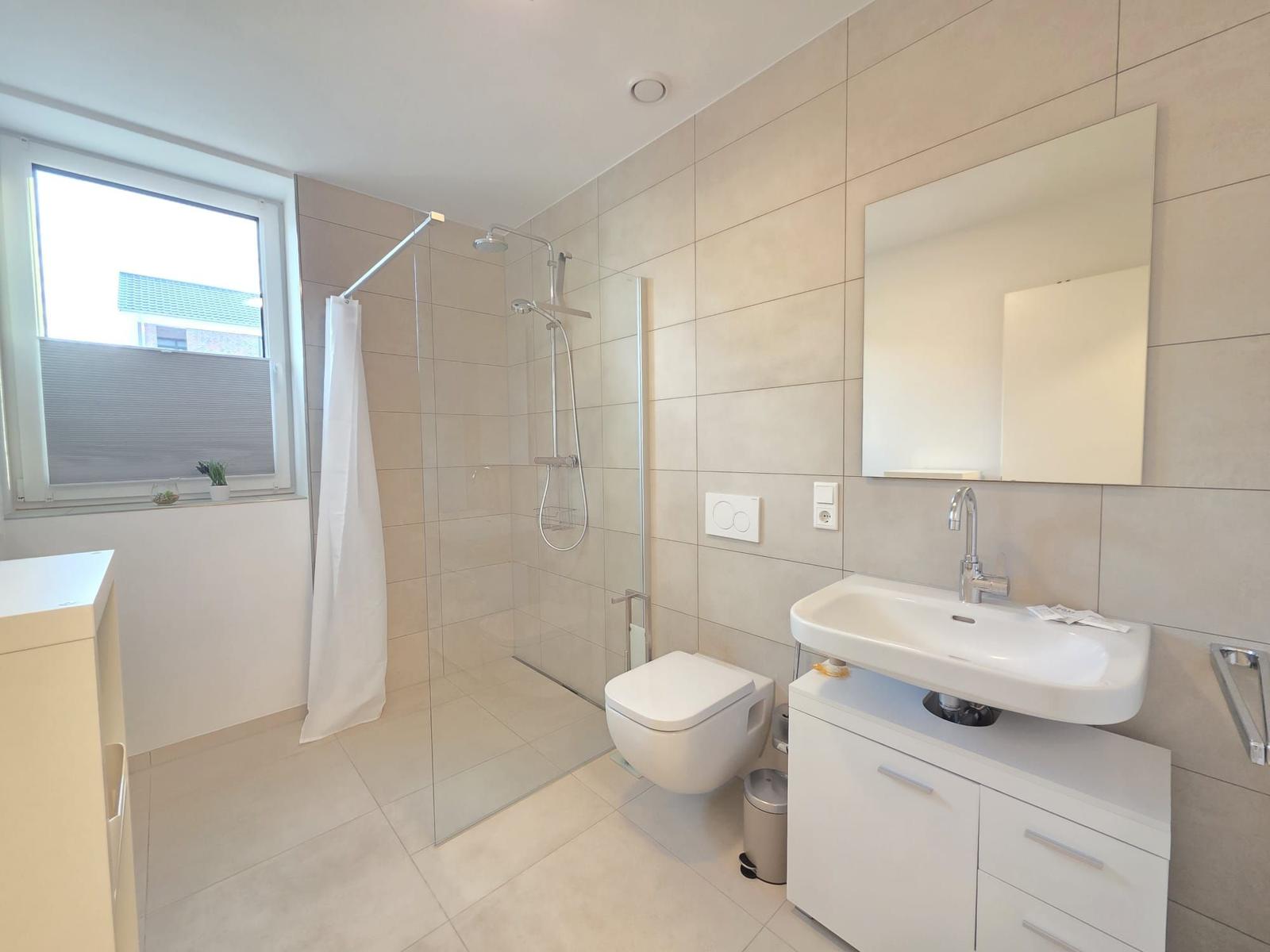 Badezimmer mit Dusche, Waschbecken und Toilette. Fenster mit Jalousie.