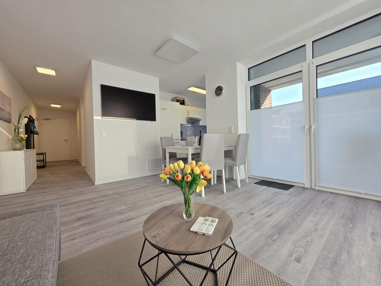 Wohnzimmer mit Essbereich, TV und Balkon. Holzboden und modern eingerichtet.