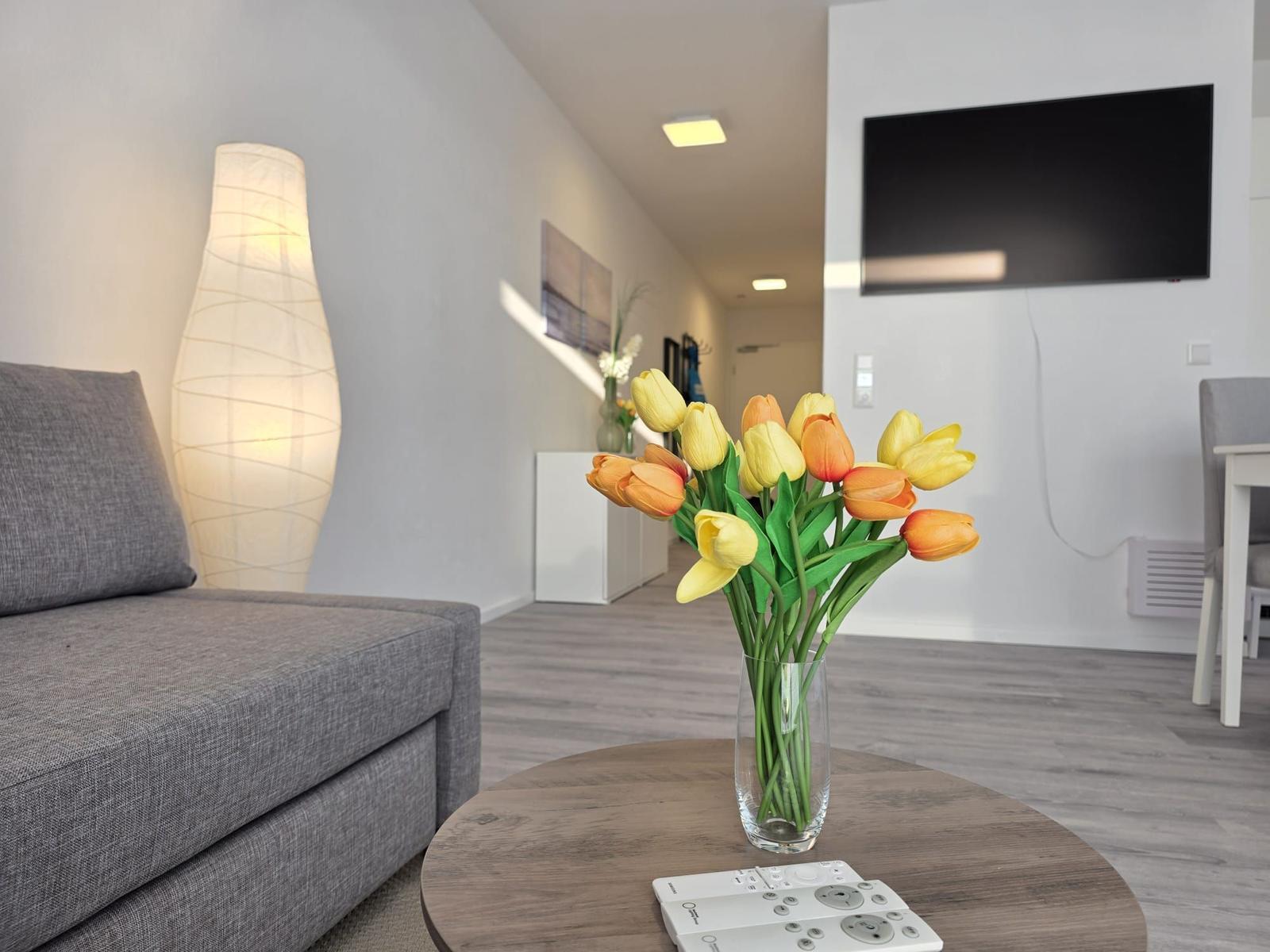 Ein Wohnzimmer mit Sofa, Fernseher und Tulpen im Vordergrund.