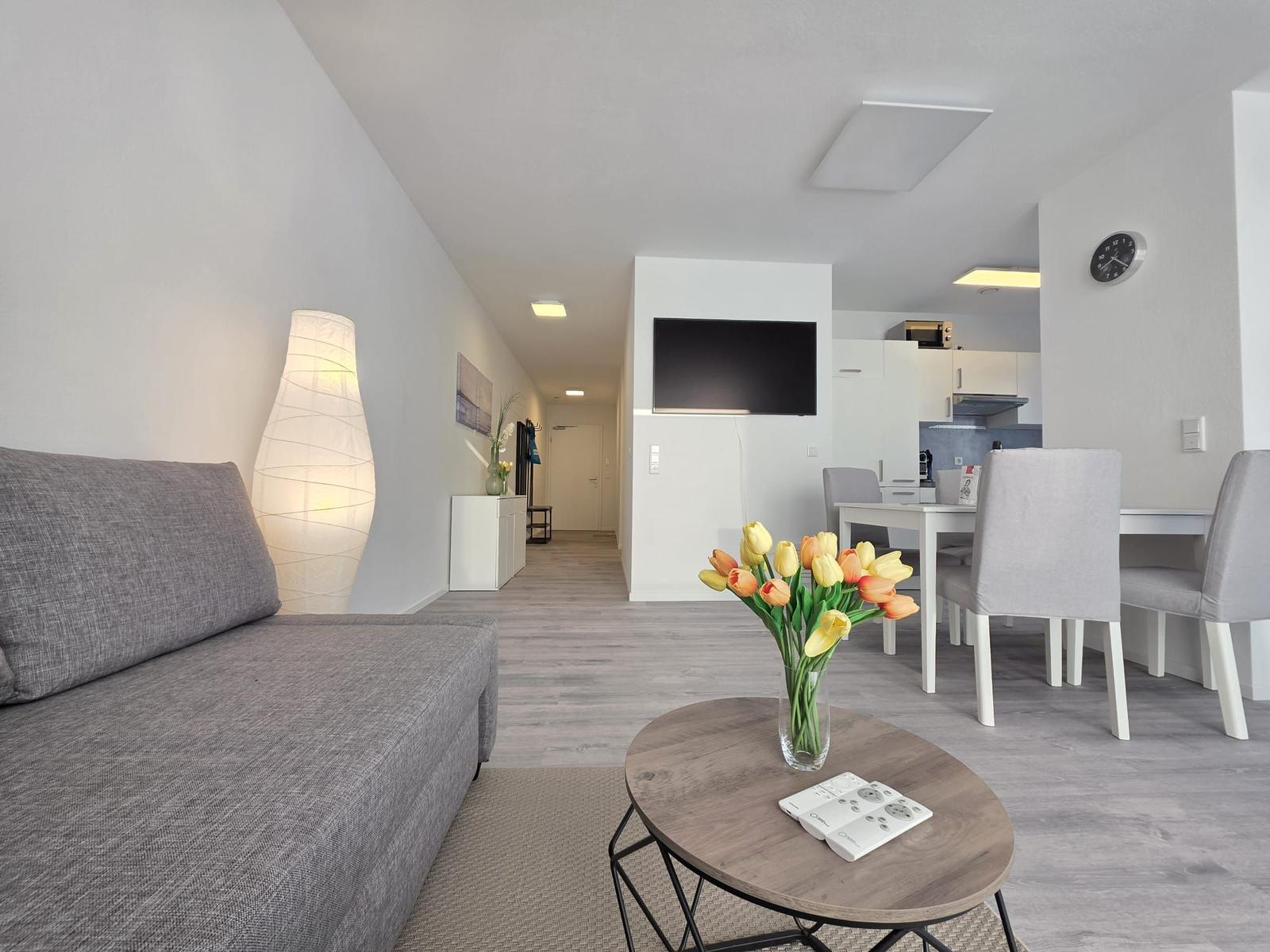 Wohnzimmer mit Sofa, Esstisch und Fernseher. Blumen auf Tisch.