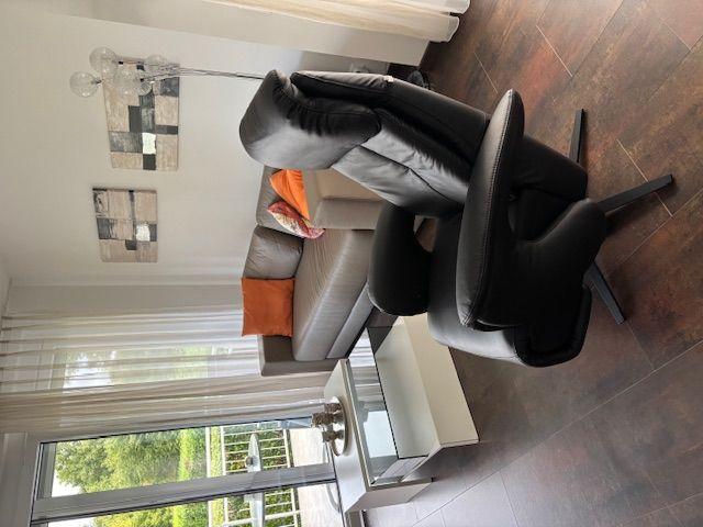 Living room with sofa, two chairs, and glass table. Access to balcony with view of greenery.