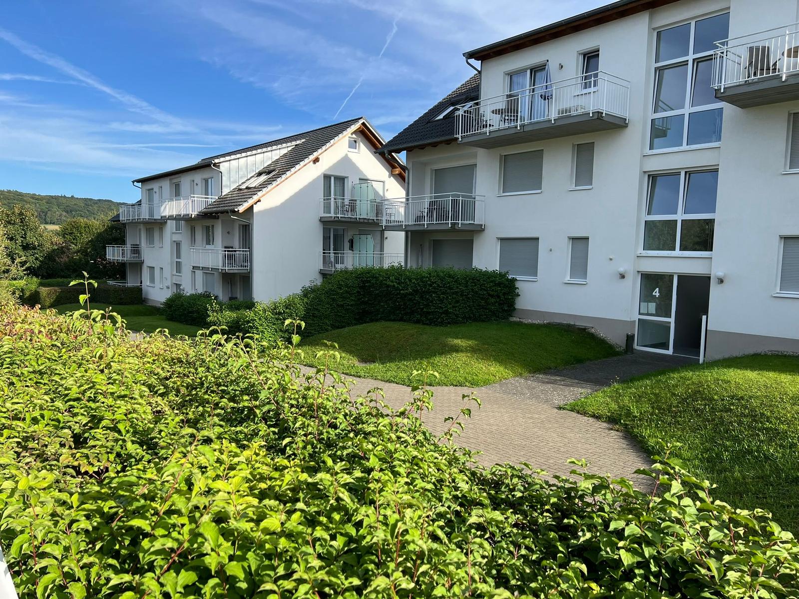 House with balconies and green garden area under blue sky.