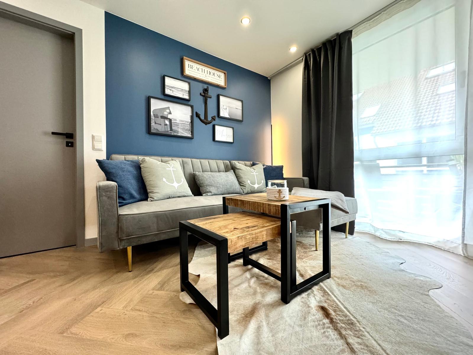 Wohnzimmer mit Sofa, Tisch und blauer Wand mit Bildern.