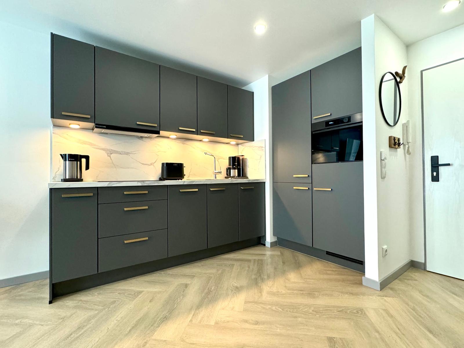 Moderne Küche mit grauen Schränken, Marmorrückwand und integriertem Ofen.