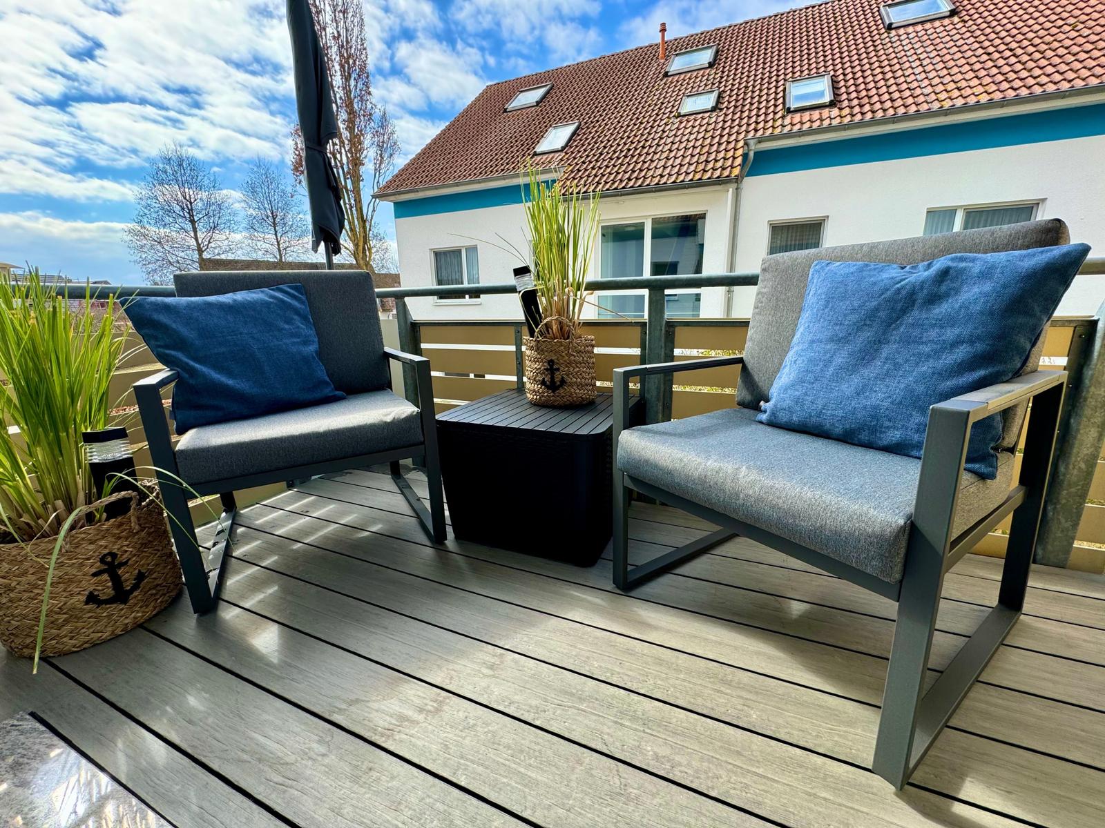 Terrasse mit zwei Sesseln, Tisch und Pflanzen. Hintergrund: Haus mit Dachfenstern.