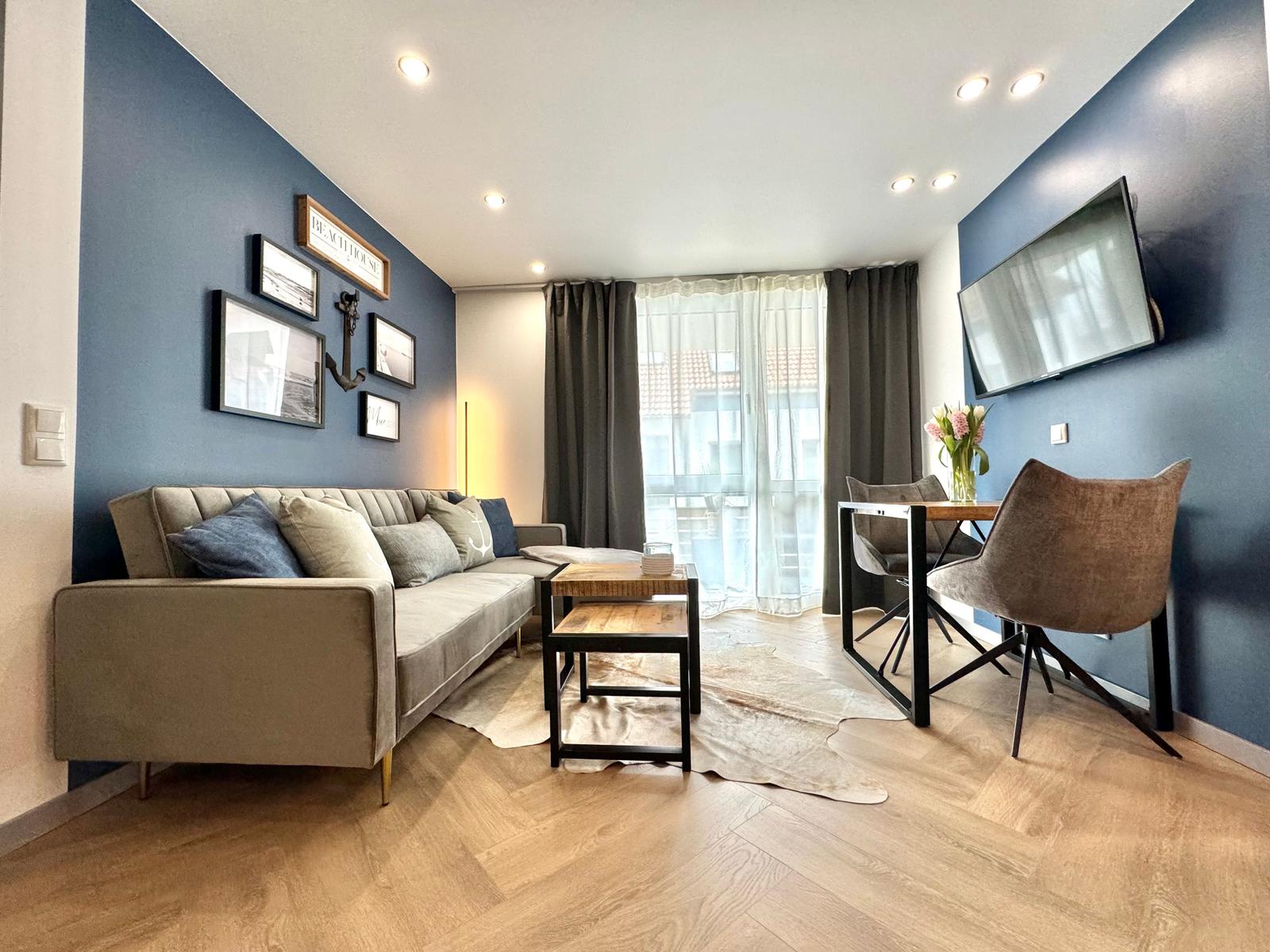 Wohnbereich mit Sofa, Esstisch und Fernseher an blauen Wänden.