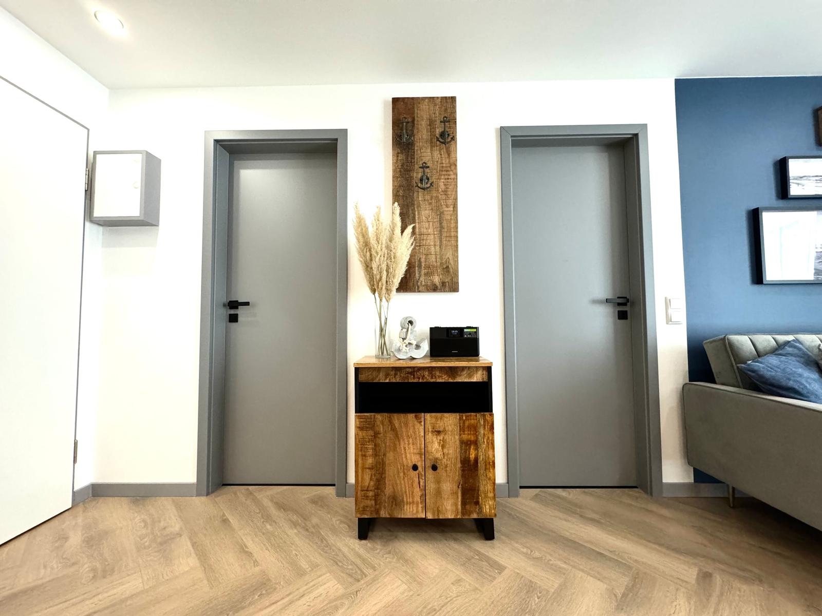 Eingangsbereich mit Holzschrank, zwei Türen und Sofa im Hintergrund.