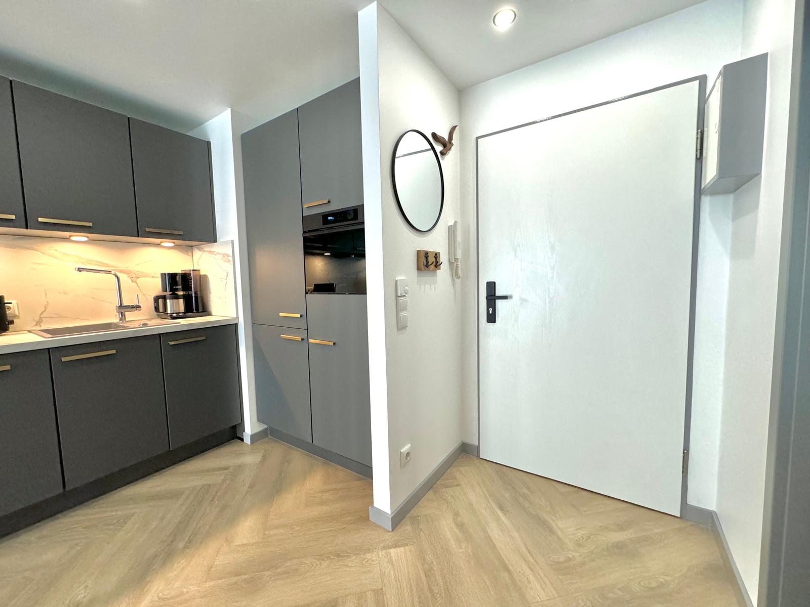 Küche mit grauen Schränken und Holzboden. Tür und Spiegel an der Wand.
