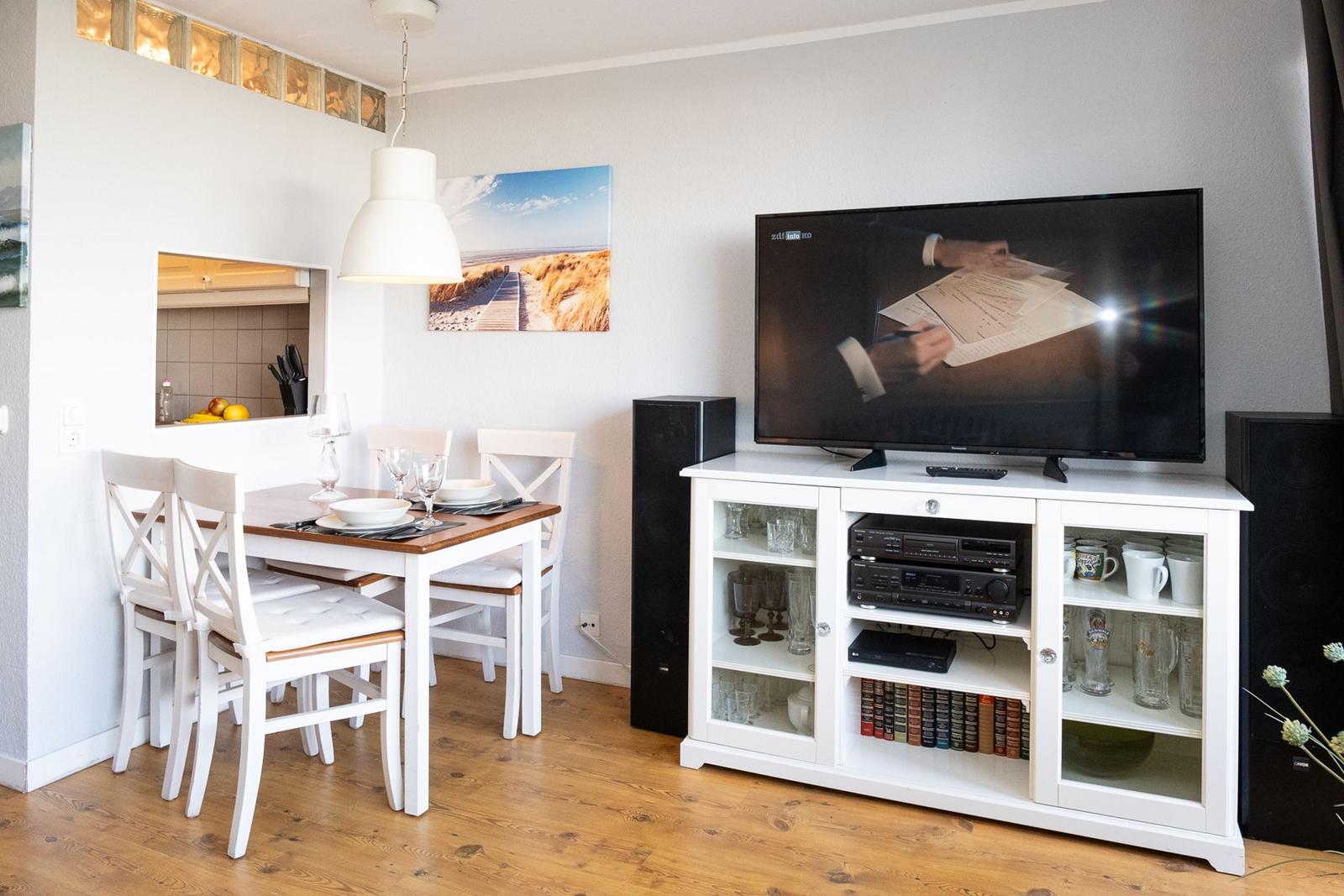 Dining area with table and chairs. TV on white cabinet with glass panels.
