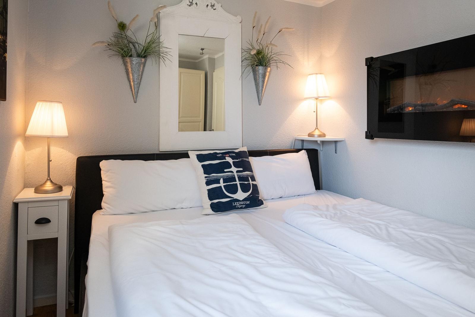 Bedroom with bed, nightstand, mirror, and wall-mounted fireplace.