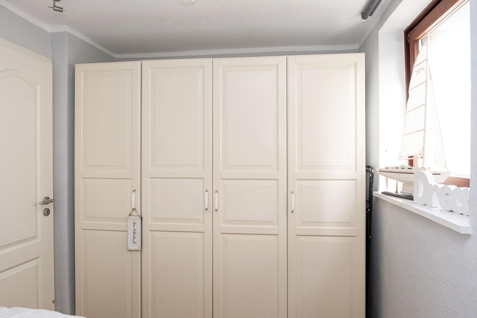 Bedroom with white wardrobe and window with sailboat model.