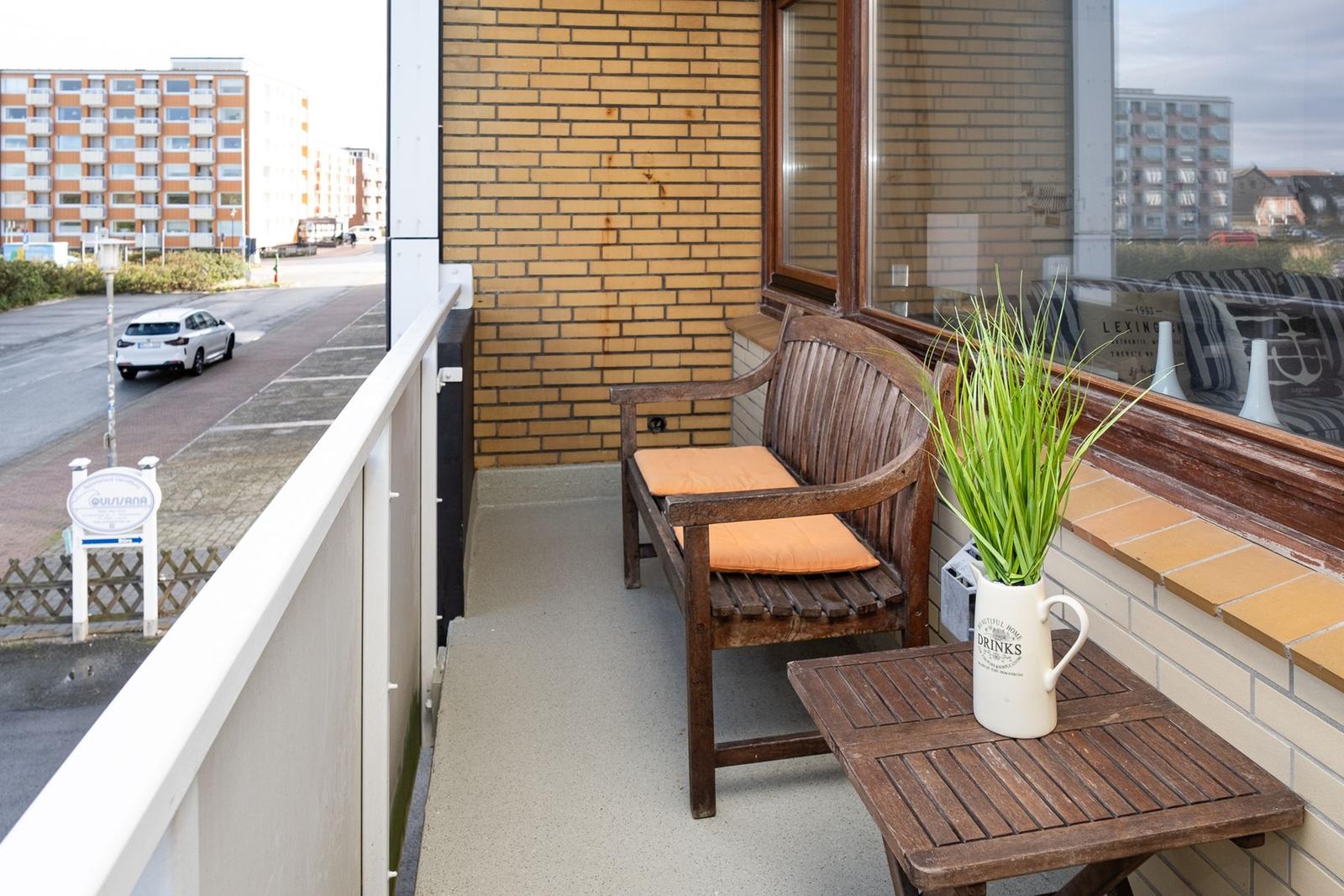 Terrace with wooden bench, orange cushions, and plant in white vase.