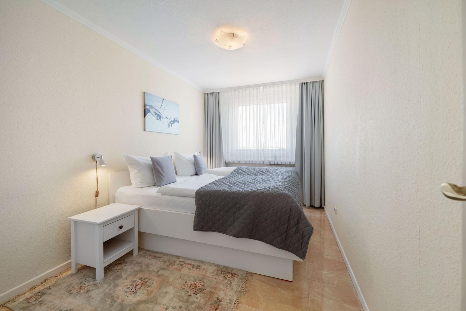 Schlafzimmer mit Doppelbett, Nachttisch und Fenster mit Vorhängen.