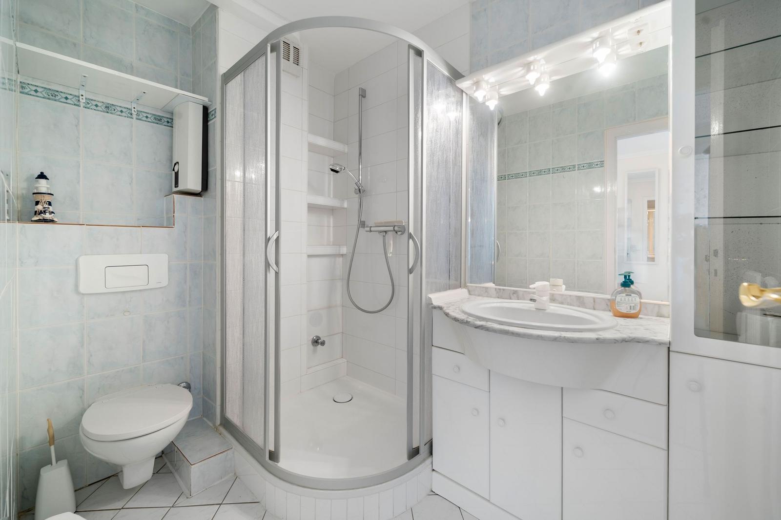 Badezimmer mit Dusche, Waschbecken und Toilette. Fliesenwand mit Mosaikstreifen.