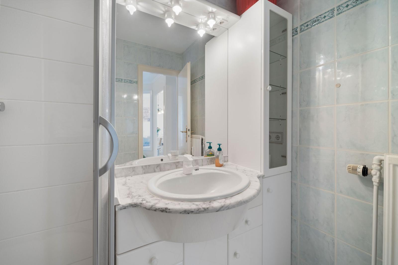 Badezimmer mit Waschbecken, Spiegel und weißen Schränken.