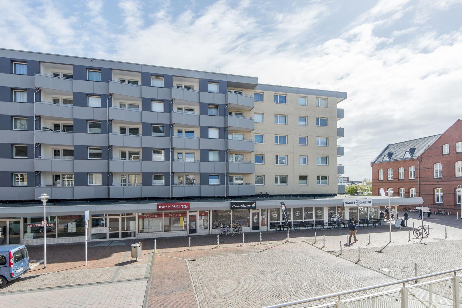 Modernes Mehrfamilienhaus mit Geschäften im Erdgeschoss und Terrassen auf den Stockwerken.