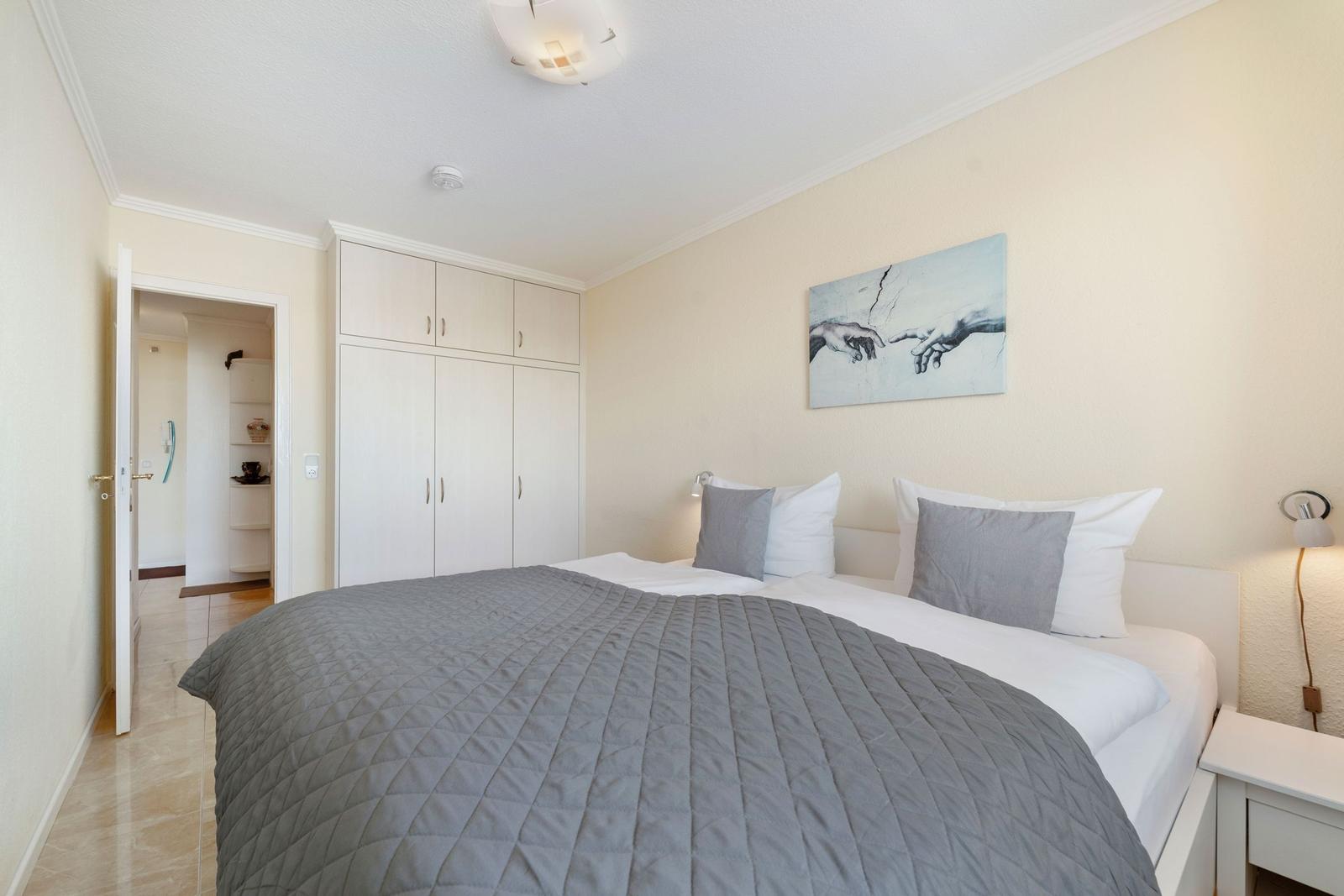 Schlafzimmer mit Bett, Kleiderschrank und Wandbild.