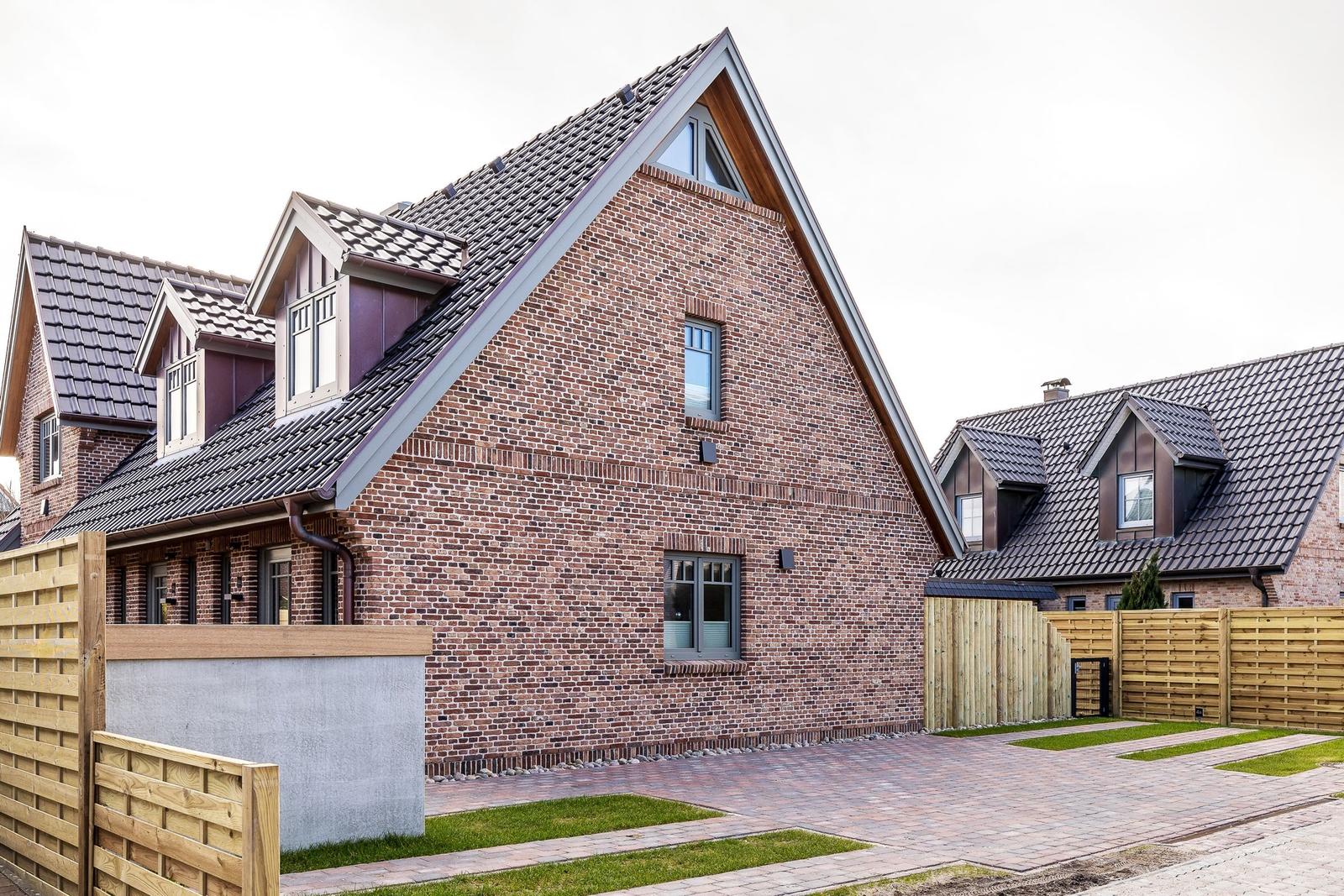 Modernes Backsteinhaus mit Dachgauben und Holzumzäunung.