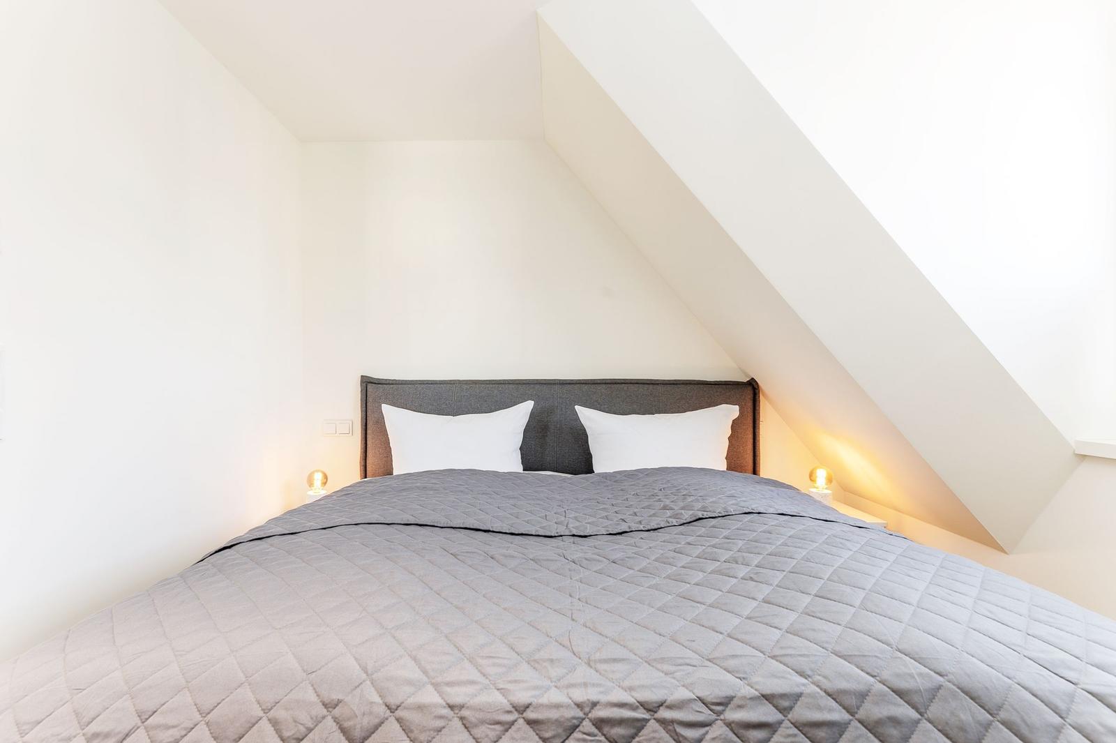 Schlafzimmer mit Dachschrägen und Bett mit grauer Bettdecke.