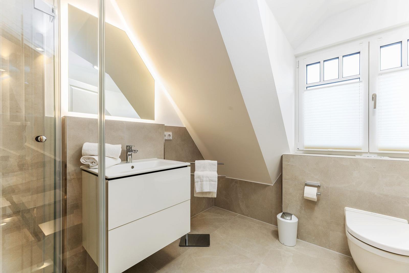 Badezimmer mit Dusche, Waschbecken und Toilette unter Dachschrägen.