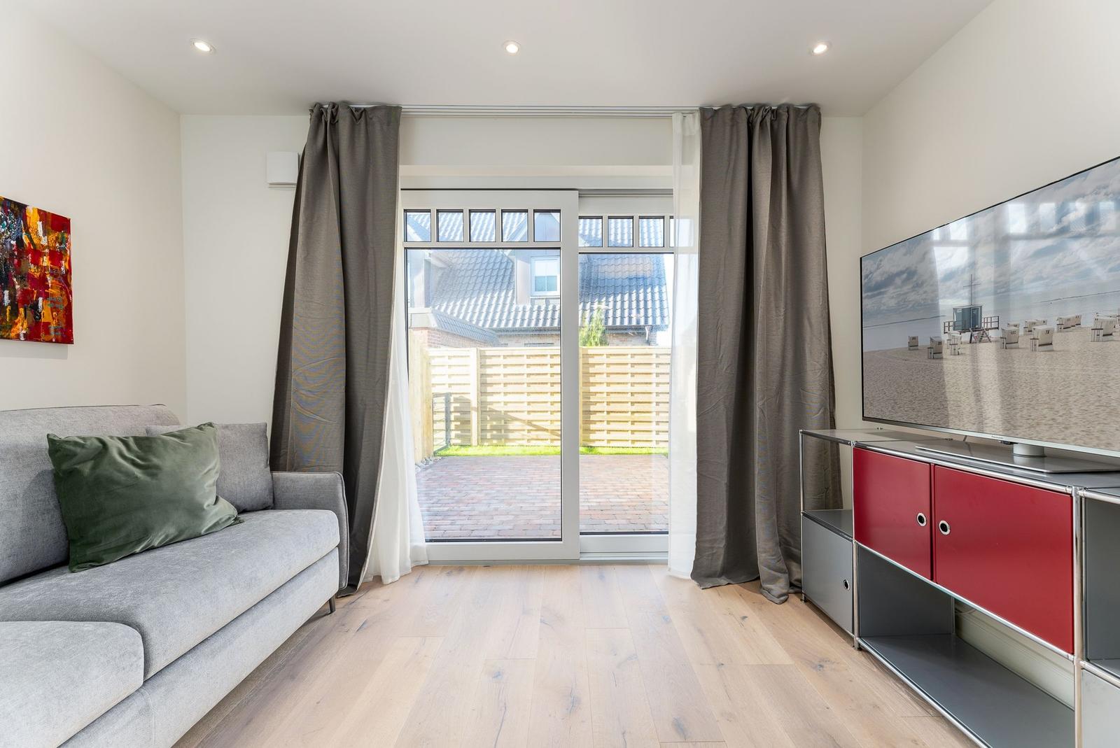 Wohnzimmer mit Sofa, Fernseher und Blick auf den Garten.