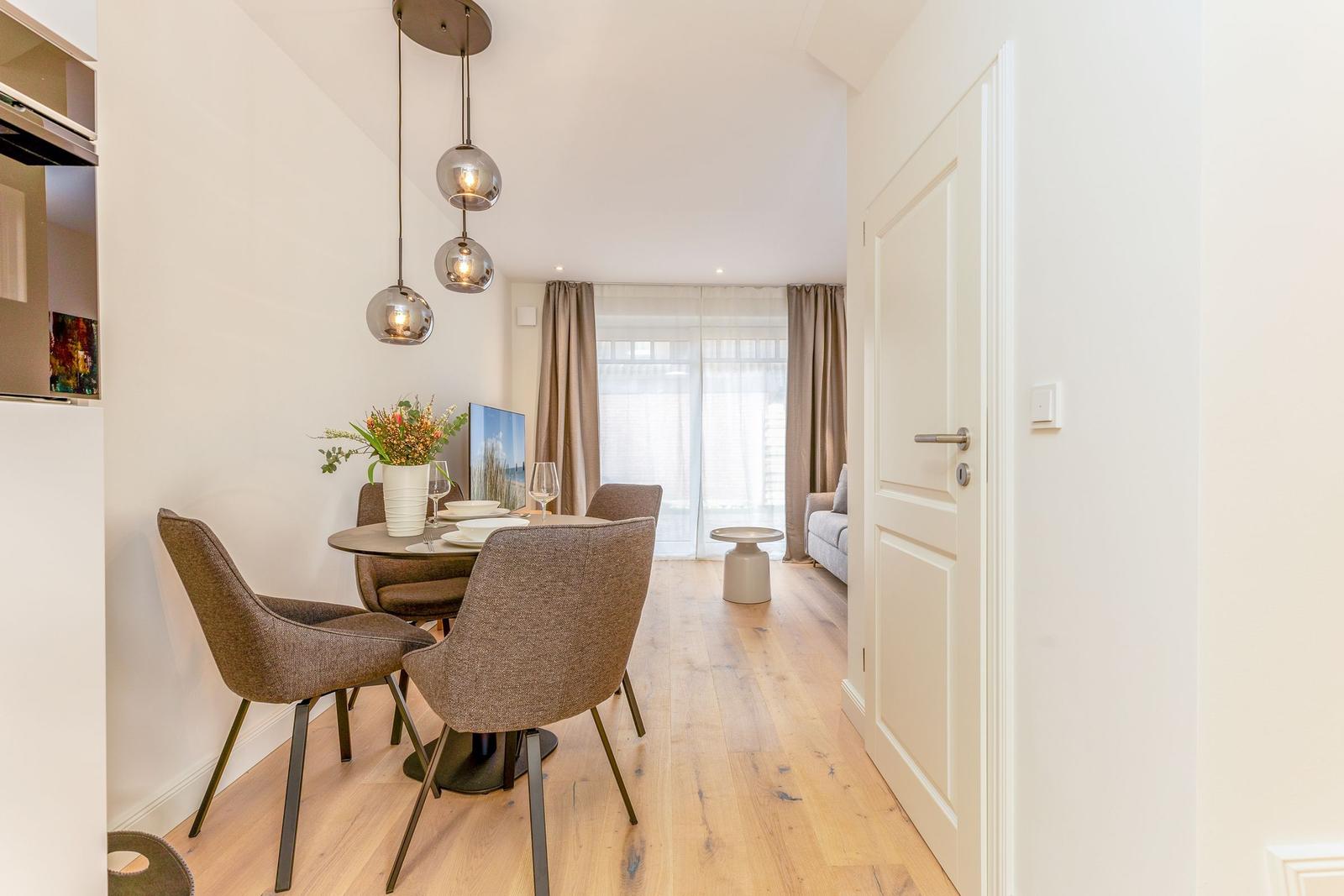 Essbereich mit Tisch, Stühlen und Hängelampen. Blick in Wohnbereich mit Sofa und Fenster.