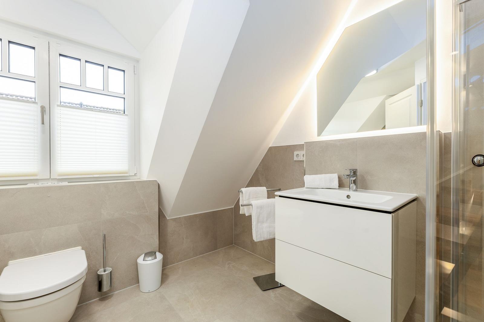 Badezimmer mit Dusche, Waschbecken und Toilette unter Dachschrägen.