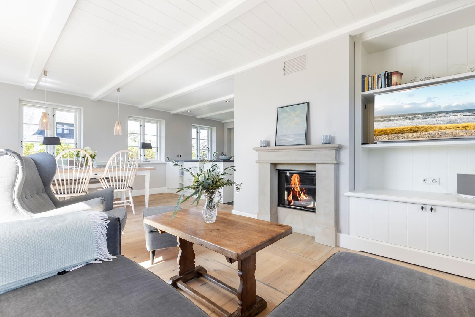 Wohnzimmer mit Kamin, TV und Essbereich. Holzboden und weiße Wände.