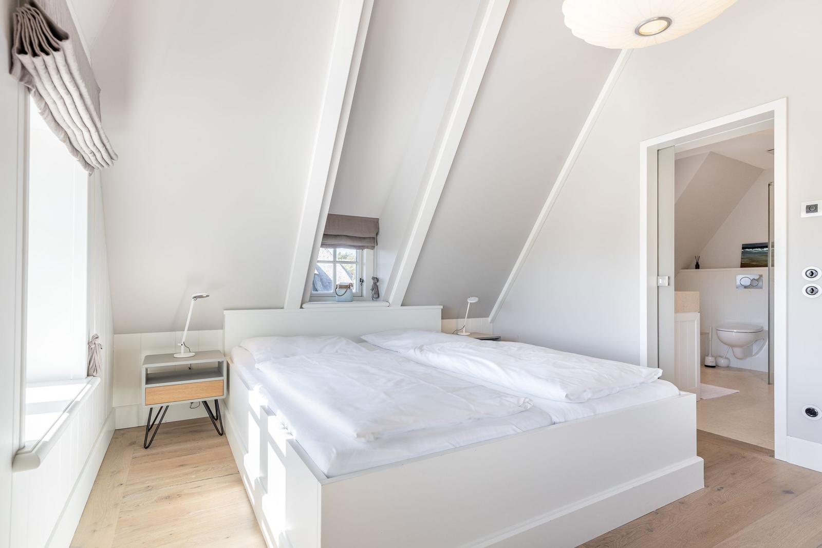 Schlafzimmer mit Doppelbett, Holzboden und Dachschrägen. Badezimmer im Anschluss.