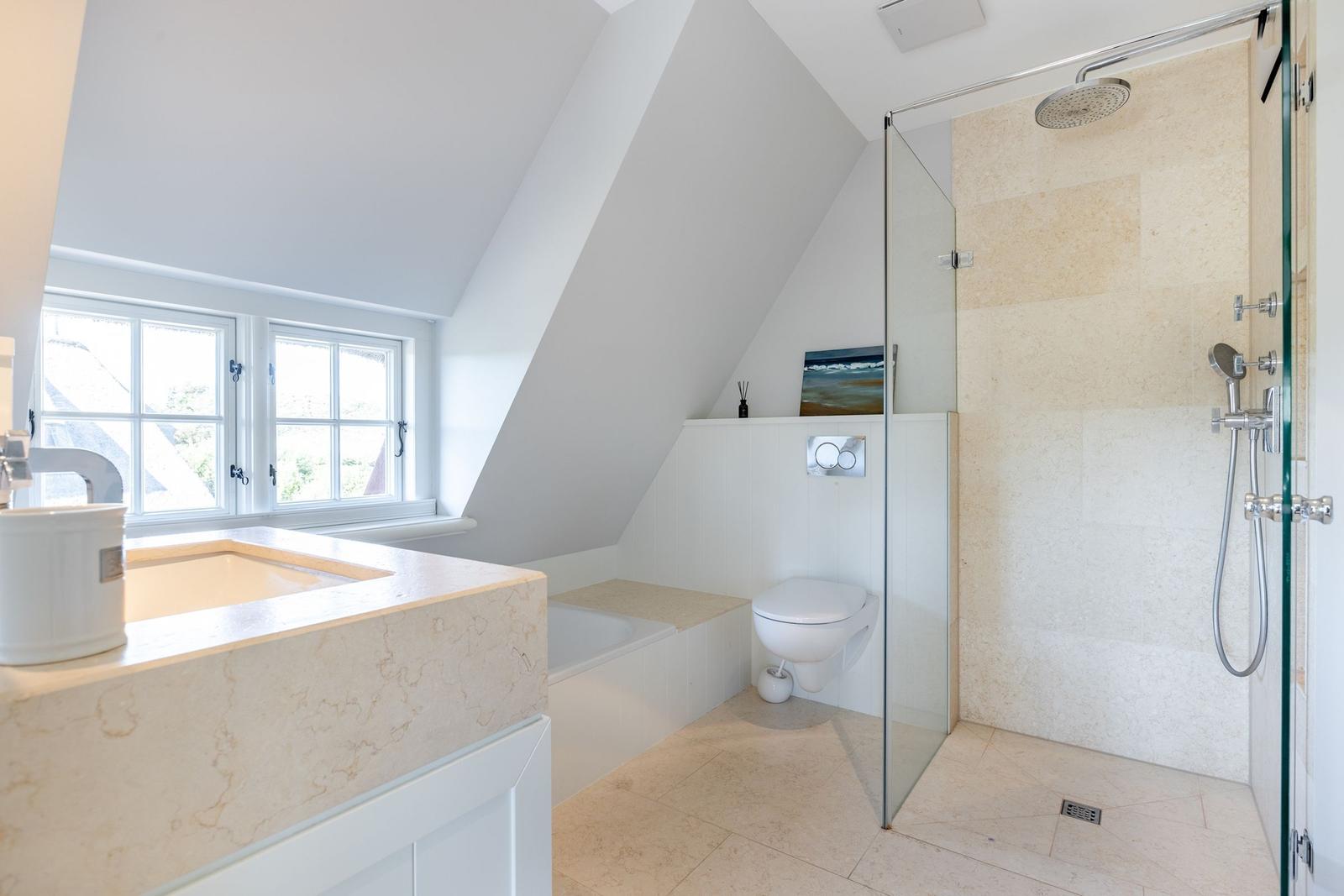 Dusche mit Glaswand, Toilette und Badewanne unter Dachschrägen mit Fenster.