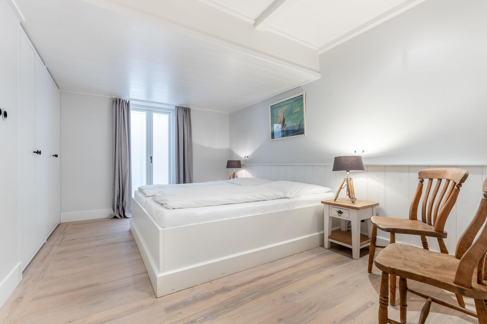 Schlafzimmer mit weißem Bett, Holzstühlen und Fenster. Wandbild und Nachttische.