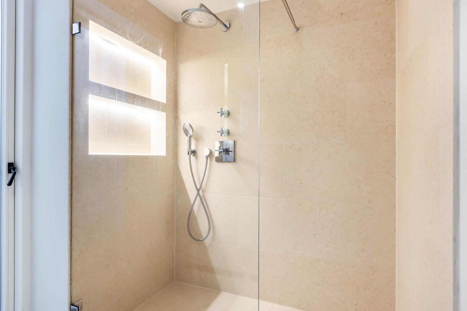 Dusche mit Glaswand, Duschbrause und beleuchteten Wandnischen.