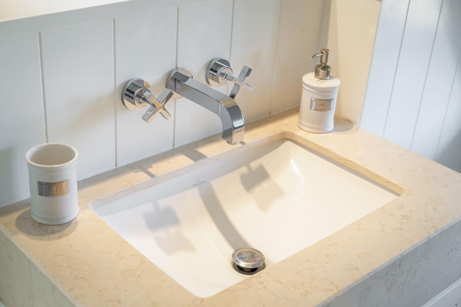 Waschbecken mit Chromarmatur und weißen Flaschen auf Marmorplatte.