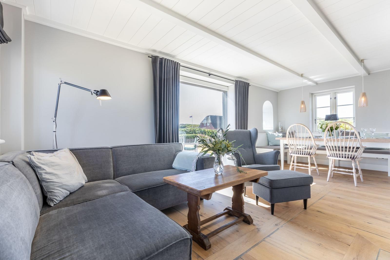 Ein Wohn- und Essbereich mit grauem Sofa, Holztisch und weißen Stühlen.
